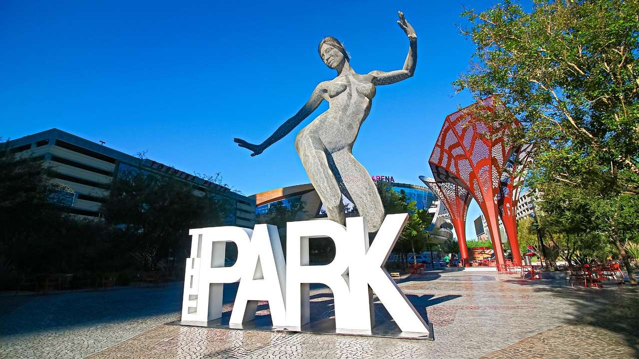A statue of a woman dancing on top of a white sign that says "Park" on a clear day