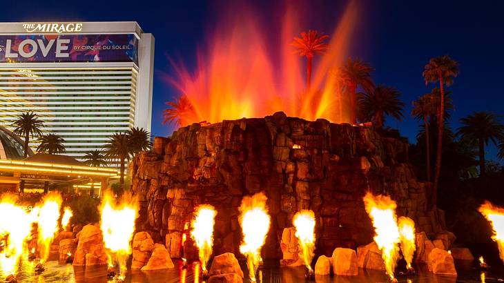 A model volcano erupting with a hotel in the background at night