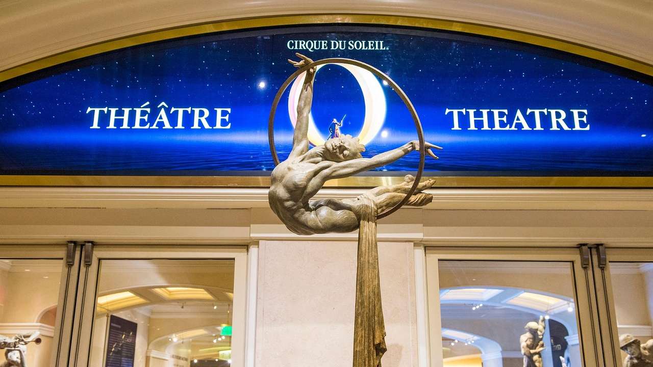 A Cirque du Soleil logo with a sculpture of an acrobat in front of it
