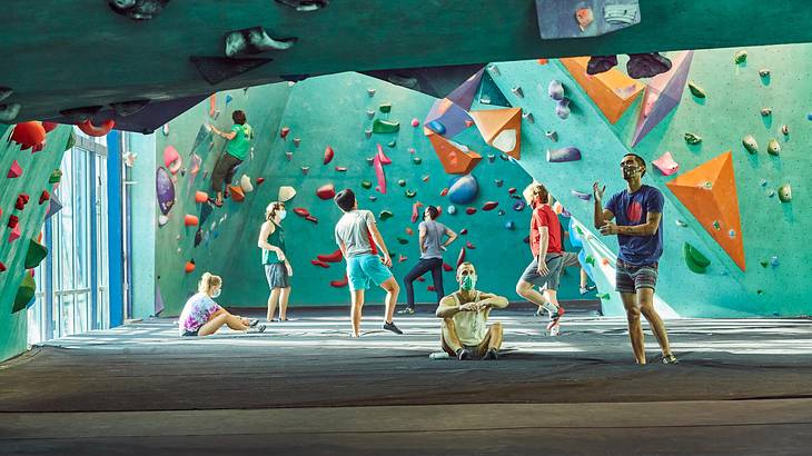 An indoor rock climbing wall with people climbing and sitting on the floor