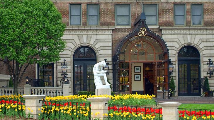 A building with a statue, tree, and tulip garden in front of it