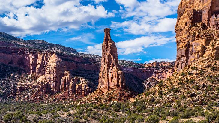 A tall sandstone tower surrounded by red rock formations under a partly cloudy sky
