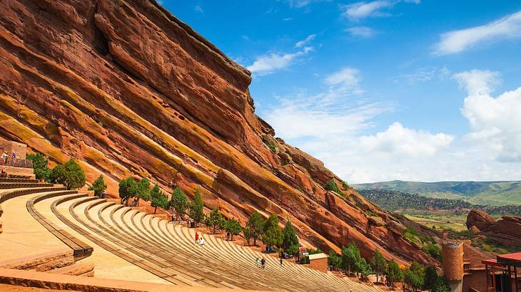 Amphitheater steps bordered by some green trees against a giant red-rock formation