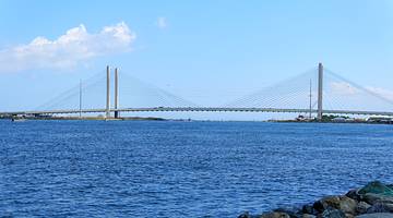 A white cable-stayed bridge over blue waters against a somewhat cloudy sky