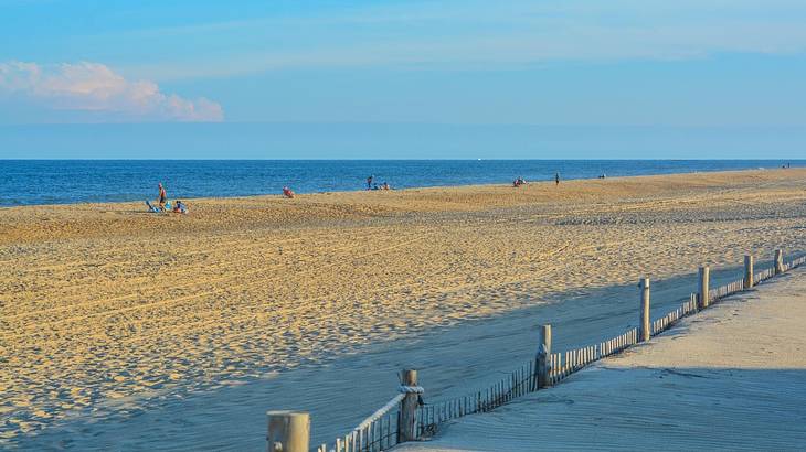 A white sand beach with people, against a sea, under a blue sky with one cloud