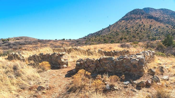 Rectangle stone ruins surrounded by brown vegetation against a hill