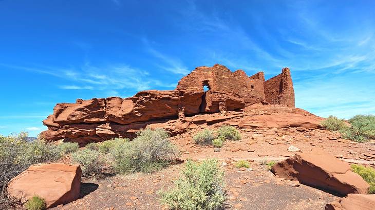 A rocky red sandstone hill with brick ruins under a partly cloudy sky