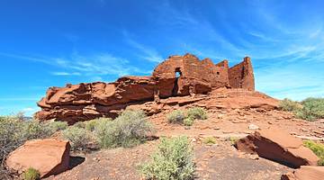 A rocky red sandstone hill with brick ruins under a partly cloudy sky