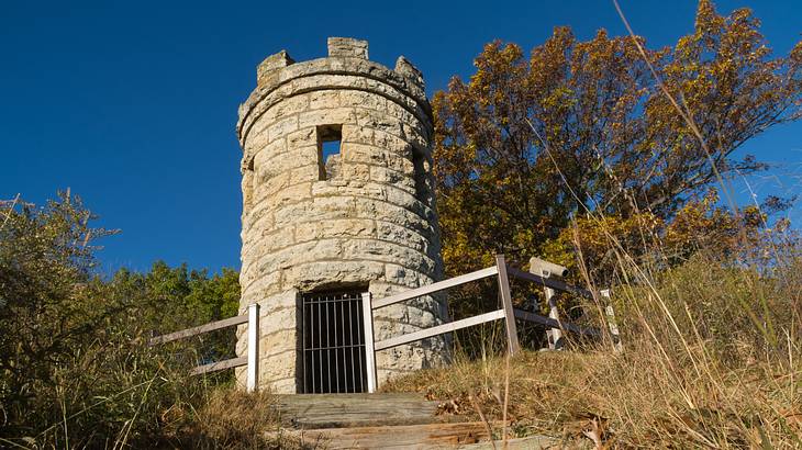 Looking up at a cylindrical stone tower behind two wooden fences