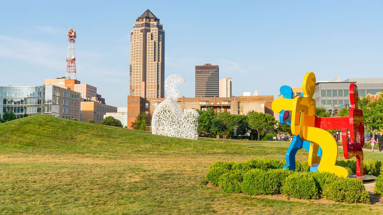 A reb, blue, and yellow sculpture of intertwined people on a green field