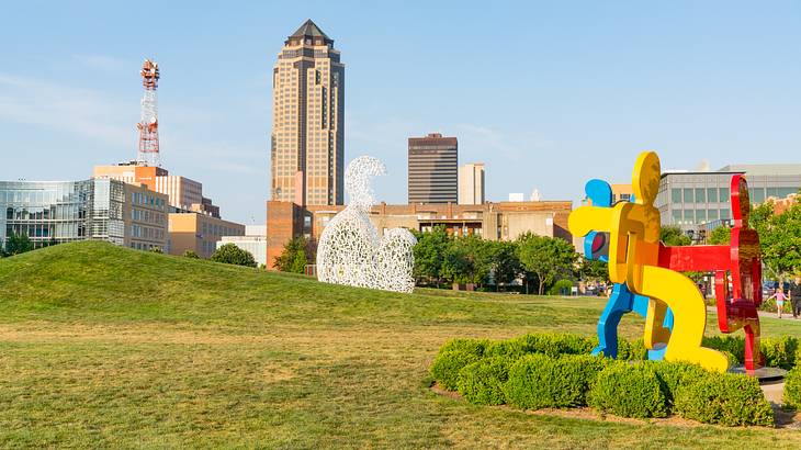 A reb, blue, and yellow sculpture of intertwined people on a green field