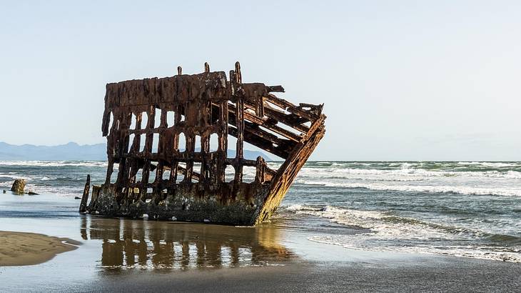 A shipwreck on the sand with ocean water surrounding it