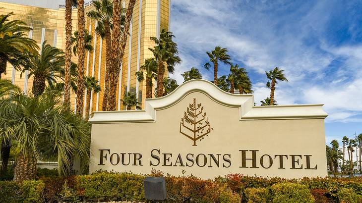 A sign that says Four Seasons Hotel with gravel in front and palm trees surrounding