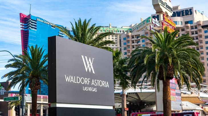 A Waldorf Astoria sign with palm trees and tall buildings behind it