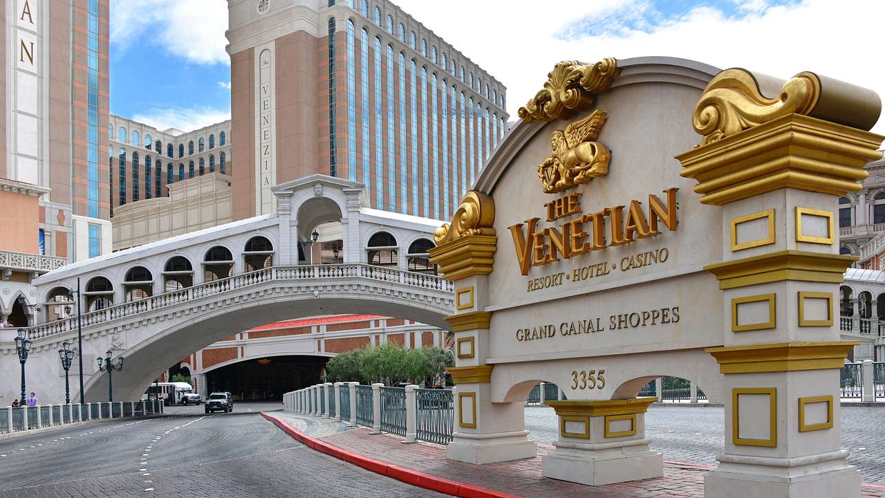A white and gold sign that says The Venetian with a bridge and buildings behind it