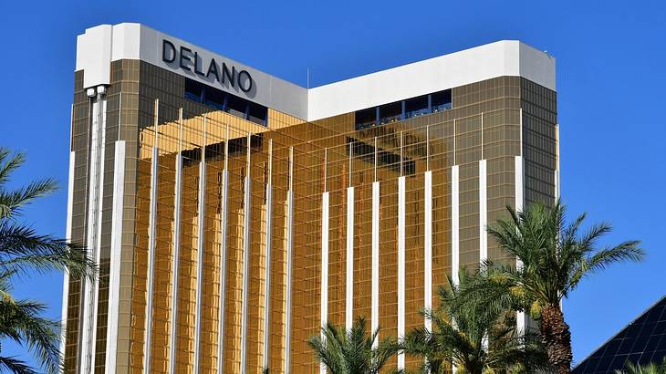 A gold mirrored building that says Delano at the top with palm trees in front
