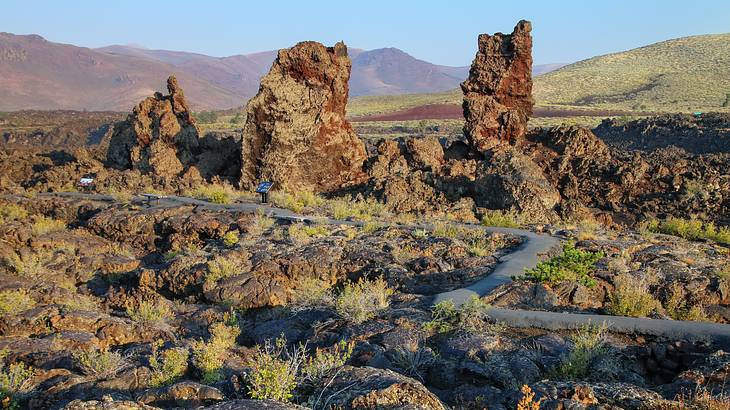 A narrow pathway winding through rugged landscapes of cinder cones and bushes A narrow pathway winding through rugged landscapes of cinder cones and bushes
