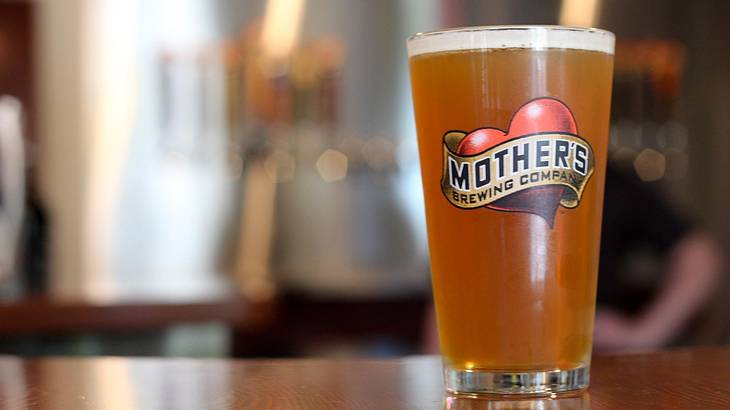 A pint of beer on a bar in a glass that says "Mother’s Brewing Company"