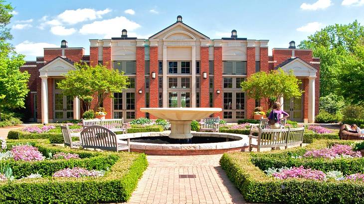 A fountain surrounded by benches and flowers against a red brick and white building