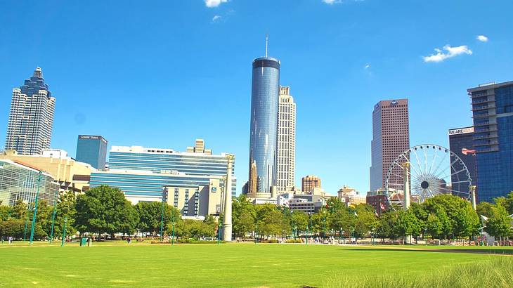 Tall skyscrapers and a Ferris wheel with green grass in front of them on a sunny day