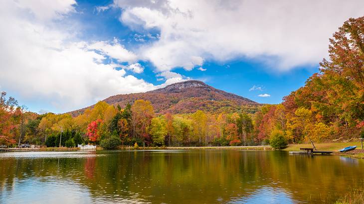 A lake against a mountain covered with autumn trees under a partly cloudy sky