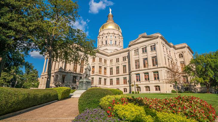 A walkway to a neoclassical building with a golden dome surrounded by a garden