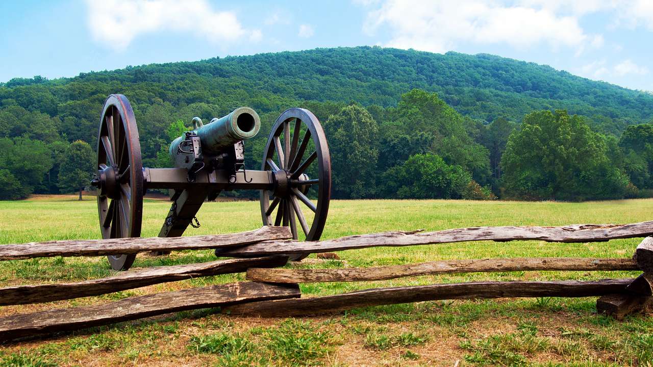 An old cannon on green grass against a mountain covered with green trees