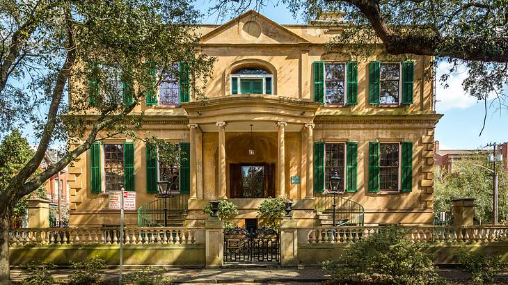 A historical building with green windows and trees and a gate in front of it