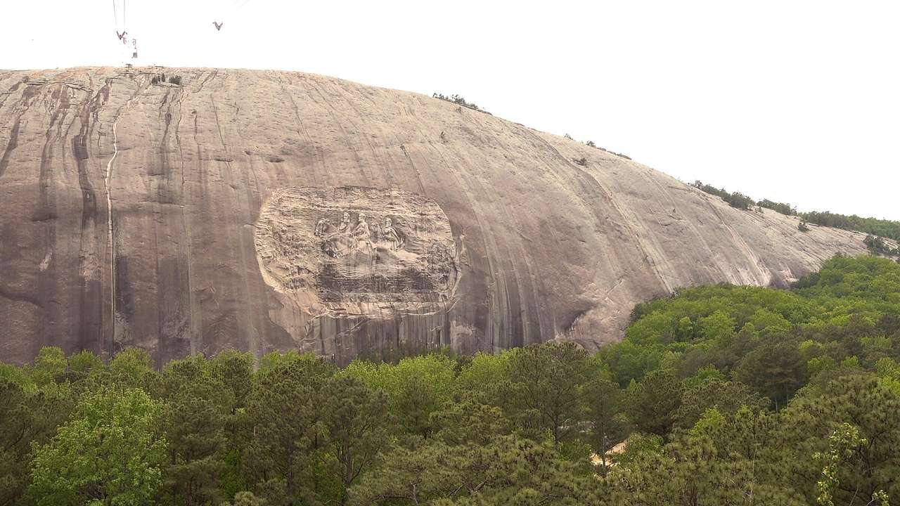 A curved smooth grey stone mountain surrounded by green trees