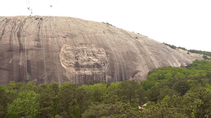 A curved smooth grey stone mountain surrounded by green trees