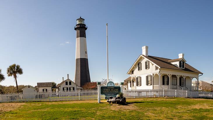 Small white houses and a tall lighthouse surrounded by a white fence and grass