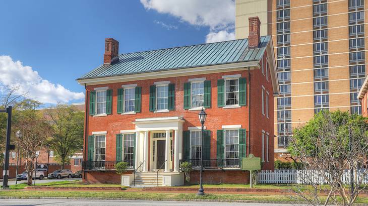 A red brick house with green window shutters and a white entrance