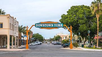 An orange and green sign that says "Downtown Yuma" on a tree-lined street