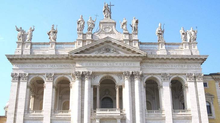 A white basilica with columns and statues and a cross on top of it