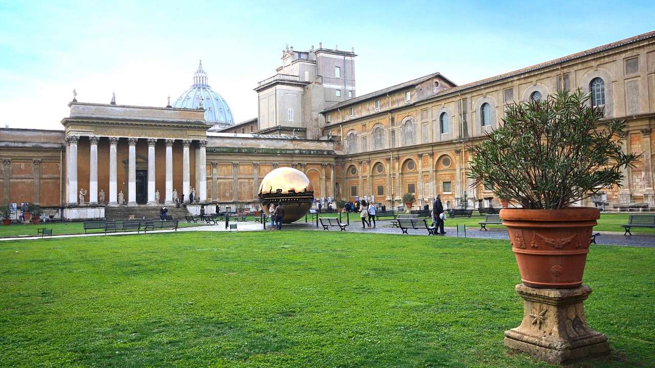 A lawn with a museum with columns and a gold sphere on the edge of it