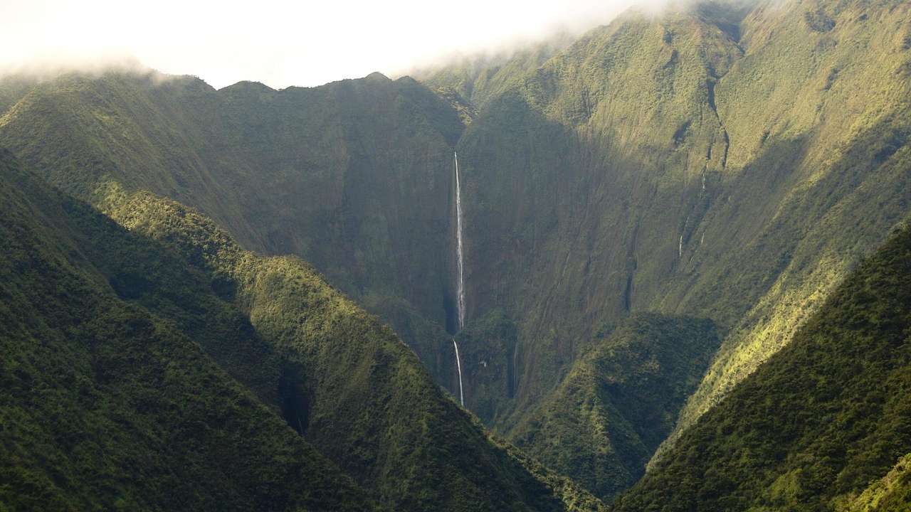 A tall and thin waterfall streaming through mountains covered in dense greenery