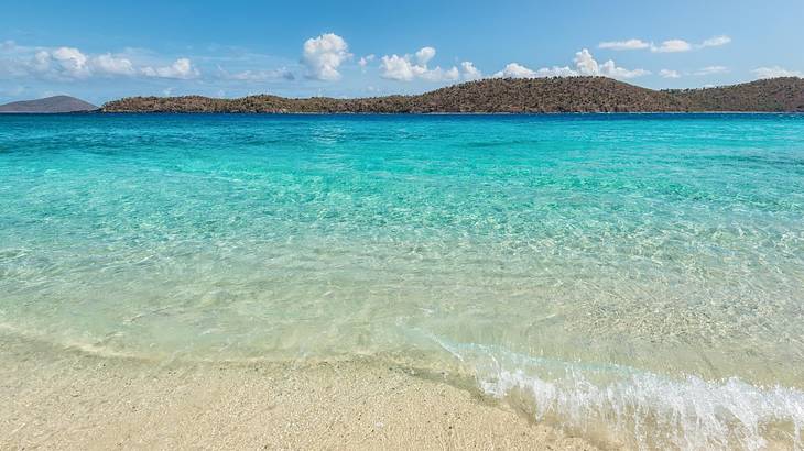 Turquoise ocean with white sand underneath it and greenery-covered cliffs in the back