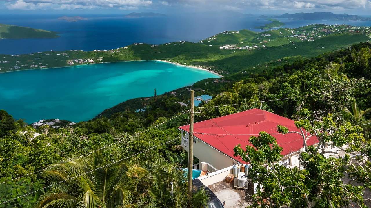 A view across an island with greenery, a turquoise bay, and a house with a red roof