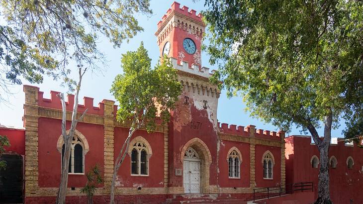 A reddish-pink castle-style building with a tower, turrets, and a clock