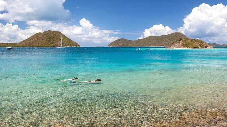 Two people snorkeling in clear water with green mountains in the background
