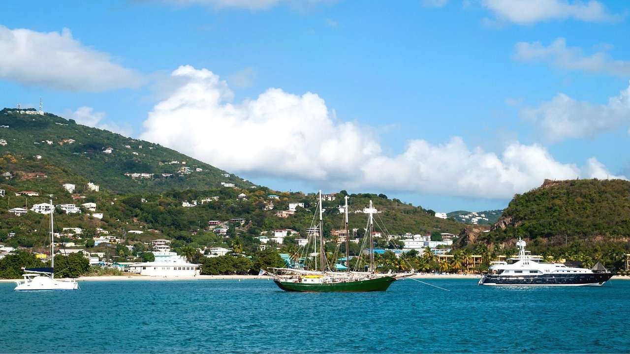 A marina with boats in it and green hills behind it under a blue sky with clouds