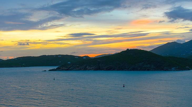 Water and green hills under an orange and blue sky at sunset