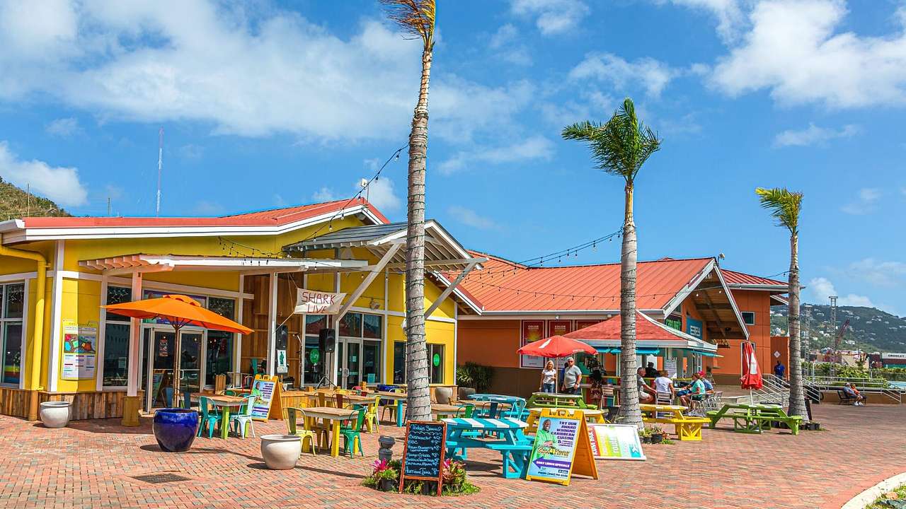 A colorful restaurant with seating and palm trees outside