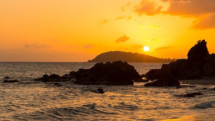 An orange sky at sunset as seen from the sea with rocks in it