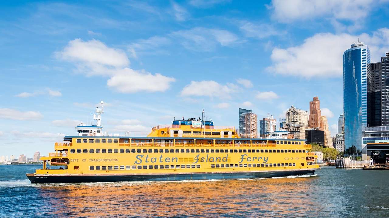 A yellow ferry that says on the water with tall buildings on the shore