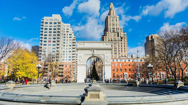 A stone arch in a square with taller buildings behind it under a blue sky