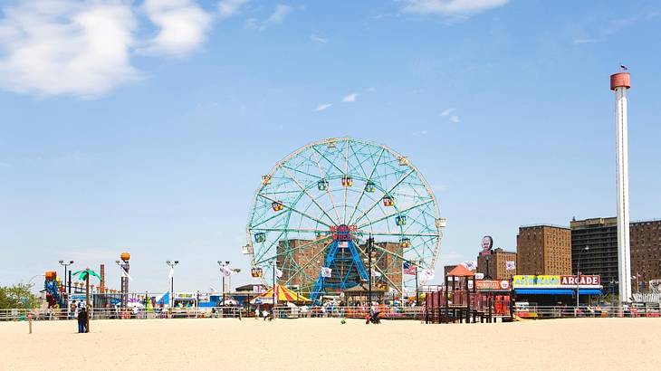A colorful Ferris wheel and other attractions with sand in front of them