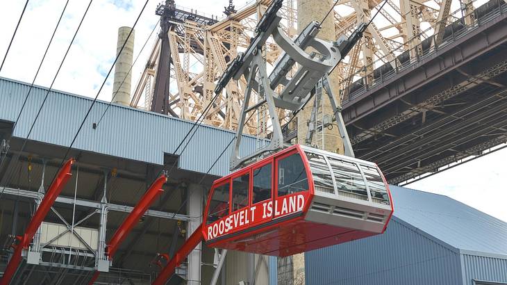 A red cable car that says "Roosevelt Island" with a bridge to the side