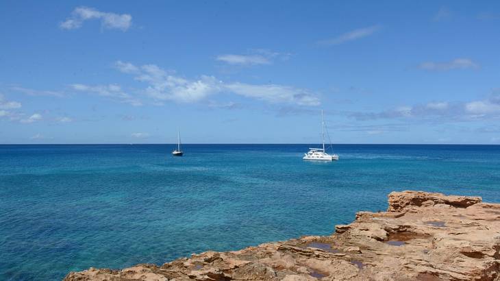 Blue sea with rocks in the foreground and two boats on the water