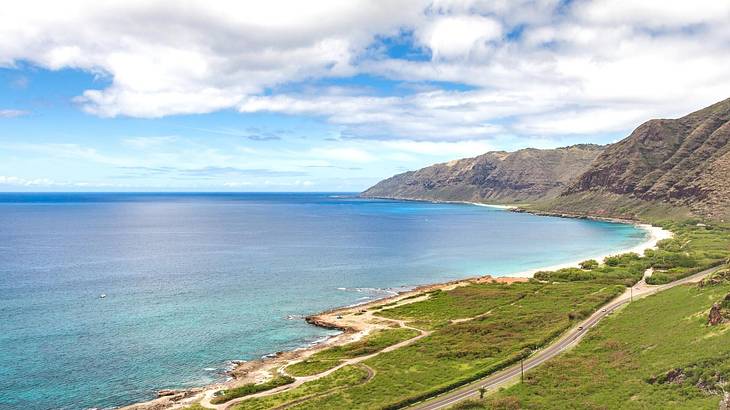 Turquoise ocean with greenery-covered mountains to the side under a blue sky